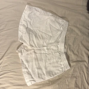 Vita linneshorts - Snygga vita linneshorts med elastisk midja för en bekväm passform. Perfekta för varma sommardagar. De är enkla och stilrena, vilket gör dem lätta att matcha med olika toppar.
