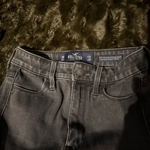 Grå jeans från Hollister - Snygga grå jeans från Hollister med hög midja och slitna detaljer vid bensluten. Perfekta för en avslappnad stil. De har en klassisk femficksdesign och knappgylf.