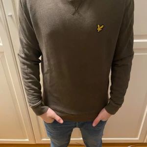 Olivgrön tröja med broderad logga - Säljer en olivgrön tröja från Lyle & Scott med broderad logga på bröstet. Tröjan har långa ärmar och en rund halsringning. Perfekt för en avslappnad stil.
