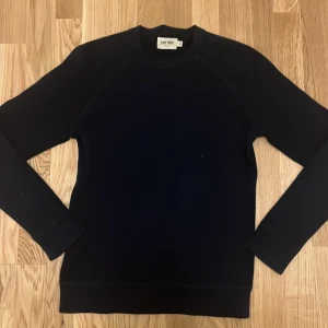 Mörkblå tröja från East West - Säljer en stilren mörkblå tröja från East West. Tröjan har en klassisk design med långa ärmar och rund halsringning. Perfekt för en minimalistisk look.