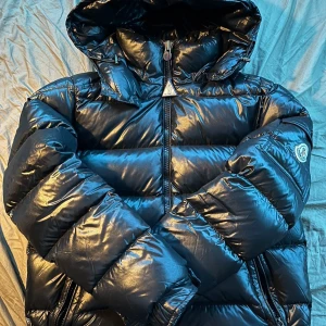 Svart dunjacka från Moncler - Säljer en snygg och varm svart dunjacka från Moncler. Jackan har en glansig finish och är perfekt för kalla vinterdagar. Den har en dragkedja framtill och en mysig huva. Perfekt för både stad och natur! 🖤
