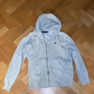 Grå zip hoodie från Ralph Lauren - Säljer en skitsnygg grå hoodie från Ralph Lauren med dragkedja och klassisk logga på bröstet. Perfekt för en avslappnad look. Passar för alla årstider. Den är S men har krympt lite i tvätten och passar även XS