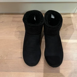 Svarta Shepard boots i mocka/läder - Säljer ett par svarta Ugg liknande boots i mocka/läder och riktig fårull inuti. Mycket fint skick och knappt använda innan de blev för små. Mycket fluff och gos invändigt. Varma och sköna. Ca 26 cm invändigt. 