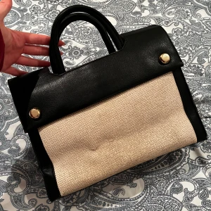 Svart och beige handväska med gulddetaljer - Snygg handväska i svart och beige med gulddetaljer. Väskan har en stilren design med svarta handtag och en beige kropp. Den har en praktisk storlek och många fack🥰