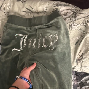 Gröna velourbyxor från Juicy Couture - Säljer ett par gröna velourbyxor från Juicy Couture med glittrande text på baksidan. Byxorna har en bekväm passform och är perfekta för en avslappnad stil. De är i bra skick och redo för nya äventyr!