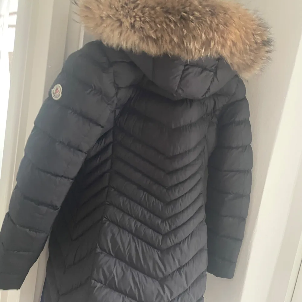 Säljer en snygg svart dunjacka från Moncler i mycket bra skick. Jackan har en fluffig pälsdetalj på huvan och en dragkedja framtill. Perfekt för kalla vinterdagar! Storleken är S/P och den är supervarm och bekväm. Passar perfekt för både vardag och festliga tillfällen.. Jackor.