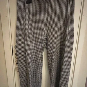 Rutig byxa från KappAhl - Snygga svartvita rutiga byxor från KappAhl i storlek L. Perfekta för både vardag och fest med sitt klassiska mönster. Byxorna har en normal passform och är gjorda i ett bekvämt material. Ett måste i garderoben för en stilren look!