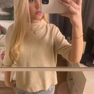 Beige stickad tröja - Säljer en superfin beige stickad tröja med trekvartsärm. Den har en hög krage som ger en mysig känsla, perfekt för kyligare dagar. Tröjan är i bra skick och passar perfekt till både jeans och kjol. Perfekt för höst och vår!