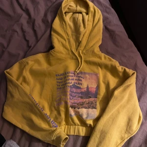 Gul hoodie med naturtryck - Betalas via swish! Säljer en supercool gul hoodie med ett tryck av naturmotiv på framsidan. Den har en skön och avslappnad passform med en stor huva och långa ärmar. Perfekt för höstmys eller chill dagar. Texten på ärmen ger den en extra touch av stil. 🏞️