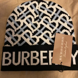 Svartvit mössa från Burberry - Snygg och stilren svartvit mössa från Burberry med deras ikoniska mönster. Perfekt för att hålla sig varm och trendig under kyliga dagar. Passar både till vardags och mer uppklädda tillfällen.