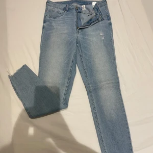 Ljusblå jeans med slitna detaljer - Snygga ljusblå jeans från Zara med slitna detaljer och råa kanter. De har en dragkedja och knapp framtill samt klassiska fem fickor. Perfekta för en avslappnad stil. Endast använda en gång!