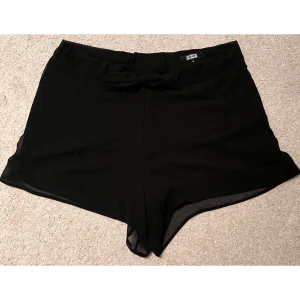 Svarta shorts från Bik Bok - Säljer ett par stilrena svarta shorts från Bik Bok i storlek S. De har en söt knytning framtill och är perfekta för både vardag och fest. 