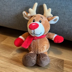 Mjuk ren med röd halsduk - Söt och mjuk ren i brunt med en röd halsduk och röda detaljer på tassarna. Perfekt som juldekoration eller mysig leksak. Renens nos är också röd, vilket ger den ett charmigt utseende.