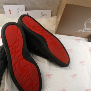 Christian Louboutin Svart - Feta svarta skor från Christian Louboutin med den ikoniska röda sulan. Skorna har en stilren design i skinn och en tyg lik sida. Perfekta för den som vill ha en lyxig touch i vardagen, 💯10/10 skick💯 säljer eftersom de inte passar, !skriv innan köp!