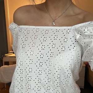 Vit offshoulder blus - Säljer en söt vit offshoulder blus med broderade blommor. Blusen har korta puffärmar och en luftig passform, perfekt för varma dagar. Den broderade designen ger en romantisk touch.