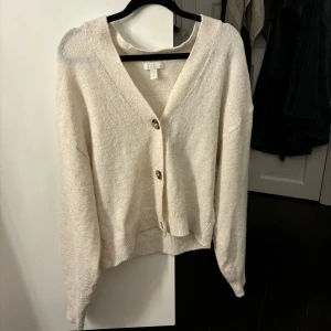 Beige kofta från H&M - Mysig beige kofta från H&M med knappar framtill. Perfekt för lager-på-lager under kyliga dagar. Den har en v-ringad design och långa ärmar. Storlek XS!