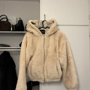Beige teddyjacka med huva - Mysig beige teddyjacka från Turkiet med huva och dragkedja framtill. Perfekt för kyliga dagar när du vill hålla dig varm och bekväm. Jackan har en avslappnad passform och är supermjuk att bära. Använd 2 gånger. 