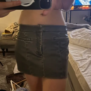 Grön skinnkjol - Säljer en snygg grön skinnkjol i kort modell. Perfekt för en utekväll eller fest! Kjolen har en stilren design med diskreta fickdetaljer framtill. Den är i bra skick och passar perfekt till en glittrig topp för en komplett look.