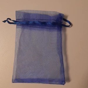 Blå organzapåse - Säljer en liten och söt blå organzapåse med dragsko. Perfekt för att förvara smycken eller små presenter. Påsen är genomskinlig och har en fin glansig yta. Perfekt för speciella tillfällen eller som en del av en presentinslagning.