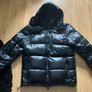 Ralph Lauren Jacka - Säljer en snygg svart dunjacka från Ralph Lauren i mycket bra skick. Perfekt för kalla vinterdagar med sin varma och puffiga design. 
