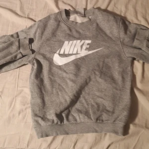 Grå sweatshirt från Nike - Säljer en grå Nike sweatshirt i storlek L. Den är i bra skick och perfekt för både träning och vardag. Tröjan har en klassisk Nike-logga på framsidan och är gjord i mjukt material för extra komfort. Passar perfekt till höst och vår!