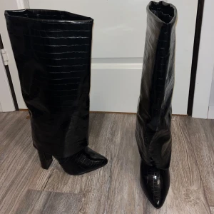Svarta stövlar med krokodilmönster - Snygga svarta stövlar i syntet med krokodilmönster och spetsig tå. De har en hög klack som ger en elegant look. Perfekta för höst och vinter, och funkar lika bra till fest som till vardags. Ett måste för garderoben! Bara använt en gång och är jätte bekväma🫶klacken är 11cm:)