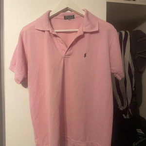 Rosa kortärmad pikétröja från Polo Ralph Lauren - Säljer en stilren rosa pikétröja från Polo Ralph Lauren med korta ärmar och klassisk krage. Tröjan har en broderad logotyp på bröstet i mörkblått. Perfekt för en avslappnad och snygg look.