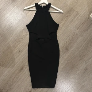Svart ärmlös klänning - Elegant svart klänning med hög hals och ärmlös design. Klänningen har en tight passform och en dragkedja i ryggen för enkel påklädning. Perfekt för en stilren look.