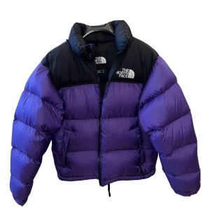 Lila och svart dunjacka från The North Face - Säljer en supervarm och snygg dunjacka från The North Face i lila och svart. Jackan har en dragkedja framtill och är perfekt för kalla vinterdagar. Den är i mycket bra skick och har långa ärmar. Perfekt för både vardag och äventyr!