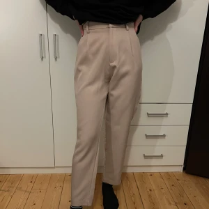 Beige kostymbyxor - Säljer ett par stilrena beige kostymbyxor i mycket bra skick. De är högmidjade och har en klassisk straight passform som passar perfekt för både vardag och fest. Materialet känns mjukt och bekvämt, vilket gör dem sköna att bära hela dagen. Perfekta för höst och vår!