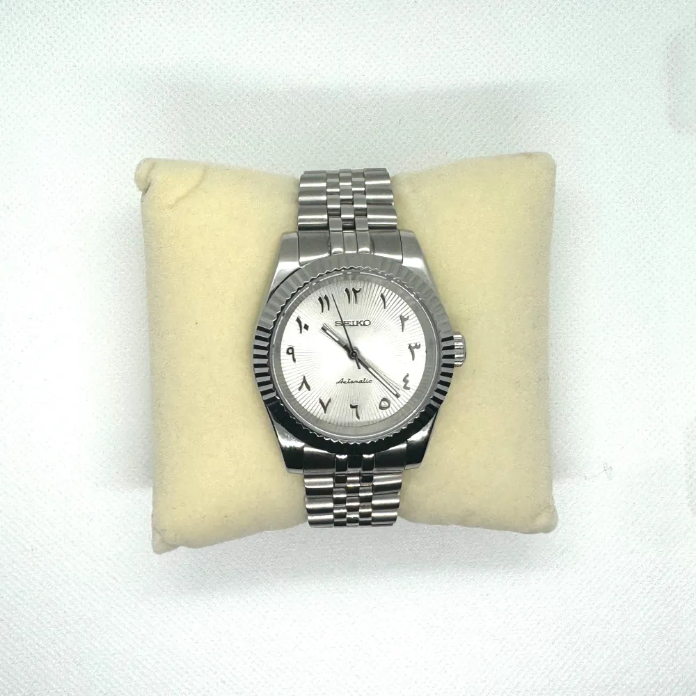 Stilren automatisk klocka från Seiko i silverfärg. Den har en klassisk design med en detaljerad urtavla och arabiska siffror. Armbandet är i rostfritt stål med en länkdesign. Perfekt för både vardag och speciella tillfällen. Klockan är stainless steel och här även en sapphire dial.. Asusteet.