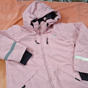 Rosa vindjacka från Funk - Säljer en rosa vindjacka och överdragsbyxor  för barn,från  Funk med huva och dragkedja. Jackan har reflexdetaljer på ärmarna och flera praktiska fickor med dragkedjor. Perfekt för blåsiga och regn dagar.
