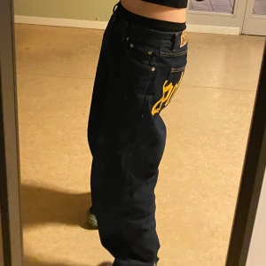 Mörkblå baggy jeans  - Mörkblå baggy jeans med en  gul textdetalj bakom. De kommer passa till de som har skate style. Finns litet grej på knän och bakom där ners. Köpte de för 800 kr. Kommer passa för de som är 165-170 tror jag. 
