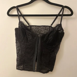 Svart spetskorsett från NA-KD - Snygg svart spetskorsett från NA-KD med justerbara axelband och vacker blommig spetsdesign. Perfekt för en stilfull look. Korsetten har en elegant och feminin touch.