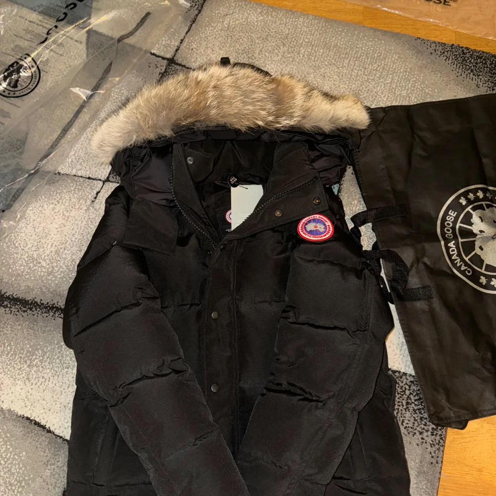 Säljer en svart dunjacka från Canada Goose i mycket bra skick. Jackan har en avtagbar pälsdetalj på huvan och är perfekt för kalla vinterdagar. Den har långa ärmar och stängs med dragkedja och knappar. Supervarm och stilren, perfekt för vintern! 🖤Pälsen är äkta vargpäls och kommer med all packetering! Tveka inte att ställa frågor!. Jackor.