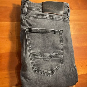 Grå jeans från Replay - Snygga grå jeans från Replay med en klassisk femficksdesign. De har en knappgylf och är i en slim passform som ger en modern look. Perfekta för en stilren vardagsoutfit. W32 L32. Modell: JOHNFRUS.