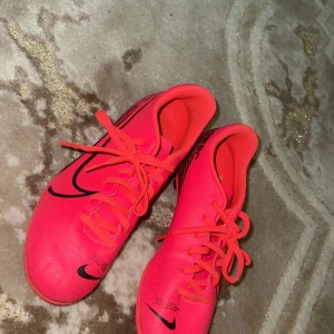 Rosa Nike fotbollsskor - Snygga rosa Nike fotbollsskor med svarta detaljer och snörning. Perfekta för fotbollsplanen med sin greppvänliga sula och stilrena design.