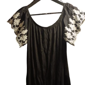 Svart singoalatop med spetsdetaljer - Elegant svart top med vackra spetsdetaljer på ärmarna. Tillverkad av en blandning av bomull och polyester, vilket ger en bekväm och lätt känsla. Perfekt för en stilfull look.