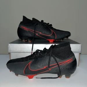 Nike Mercurial Superfly 7 FG - Snygga svarta fotbollsskor från Nike med röda detaljer och snörning. Skorna har en strömlinjeformad design med hög ankel för extra stöd. Perfekta för fotbollsplanen med sin slitstarka syntetiska yta och greppvänliga dobbar. 8/10 skick (priset kan diskuteras!)