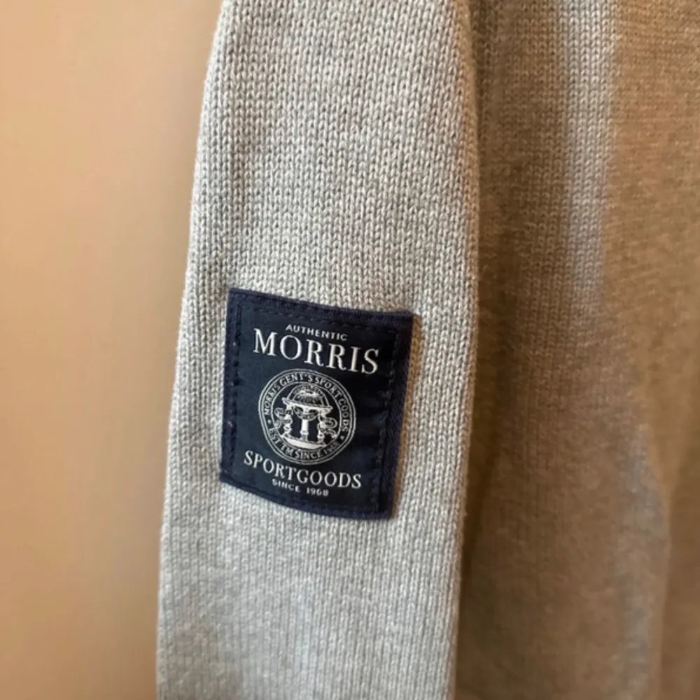 Snygg grå tröja från Morris med ett mörkblått band över bröstet där märket och en brittisk flagga är broderade. Tröjan har långa ärmar och en ribbad krage samt muddar. Perfekt för en stilren och avslappnad look.. Tröjor & Koftor.