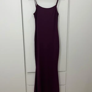 Mörklila långklänning - Elegant mörklila långklänning med smala axelband. Perfekt för en stilren look. Klänningen har en enkel och tidlös design.