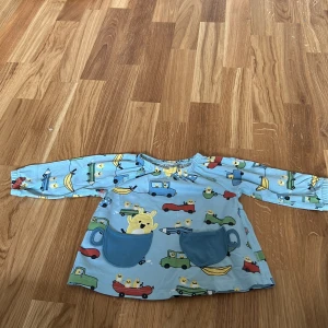 Blå långärmad tröja med bilmotiv från Polarn O. Pyret - Söt blå långärmad tröja från Polarn O. Pyret med färgglada bilmotiv och praktiska fickor framtill. Perfekt för små äventyrare! Tillverkad i mjukt material för bekväm passform.