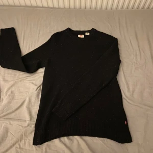 Svart stickad tröja från Levi's - Säljer en snygg svart stickad tröja från Levi's i storlek M (passar även S bra då den är lite åt de tightare hållet). Tröjan har ett diskret mönster med små färgprickar och är perfekt för både höst och vinter.  Jättesnygg och prisvärd. Nypris ligger runt 800-900kr