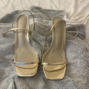 Champagne färgade klackskor från Boohoo - Snygga champagne färgade klackskor från Boohoo i storlek 38. De har en elegant design med smala remmar och en fyrkantig tå. Perfekta för festliga tillfällen när du vill glänsa lite extra. Skorna är i mycket bra skick och redo att användas på nästa party!