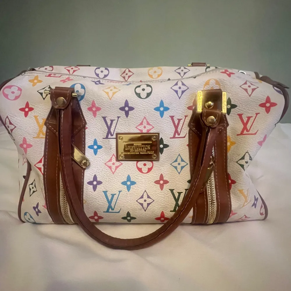 Säljer en superfin flerfärgad handväska från Louis Vuitton med deras ikoniska monogrammönster. Väskan har bruna läderhandtag och en snygg guldfärgad platta framtill. Perfekt för att ge din outfit en lyxig touch! 👜✨. Laukut & Käsilaukut.