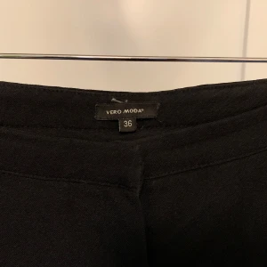 Högmidjade byxor från Vero Moda - Säljer ett par stilrena svarta byxor från Vero Moda i storlek 36. De har en klassisk design med en rak passform och hög midja. Perfekta för både vardag och festliga tillfällen. Materialet känns mjukt och bekvämt. Passar utmärkt till en snygg blus eller en enkel t-shirt.