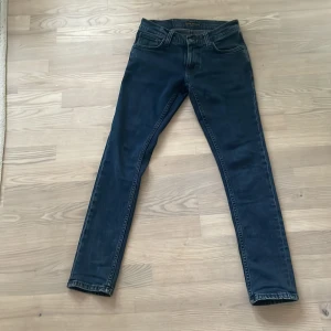 Mörkblå jeans från Nudie Jeans - Säljer ett par snygga mörkblå jeans från Nudie Jeans. De har en klassisk femficksdesign och är i storlek 27/30. Jeansen har en slim passform och är perfekta för både vardag och fest. De är i bra skick och redo för en ny ägare! Modell tight terry, nypris 1600.