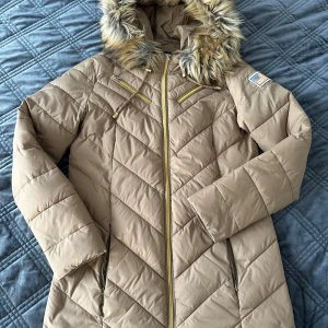 Beige pufferjacka från Svea - Snygg beige vinterjacka från Svea. Storlek är Small/Medium. Jackan har en mysig huva med fuskpäls som är riktigt fin och en praktisk dubbelsidig dragkedja framtill. Pälsen kan även tas bort. Perfekt för kalla vinterdagar! 🧥❄️