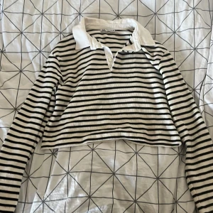 Randig croppad tröja från Zara - Säljer en superfin randig tröja från Zara. Den är svart och vit med långa ärmar och en klassisk krage. Tröjan är croppad vilket ger den en modern look. Perfekt för både vardag och fest!