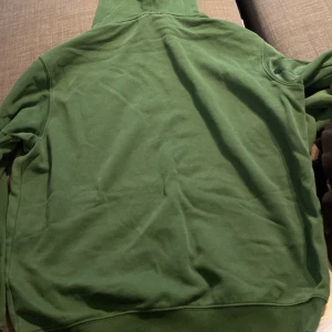 Grön hoodie - Säljer en grön hoodie i bra skick. Den har en klassisk känguruficka och en justerbar huva med snören. Perfekt för en avslappnad stil och passar bra till både vardag och chill.